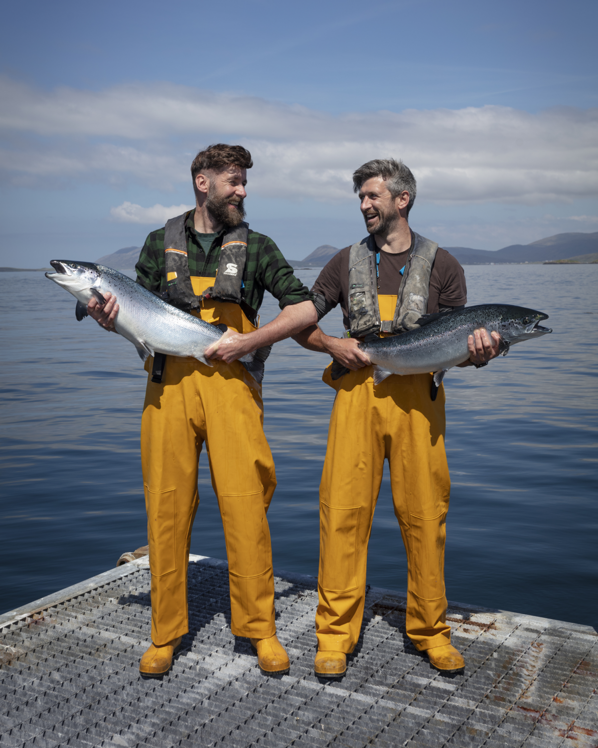 Two men hold salmon on a farm site