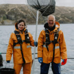 Two salmon workers standing with a large net on a farm site